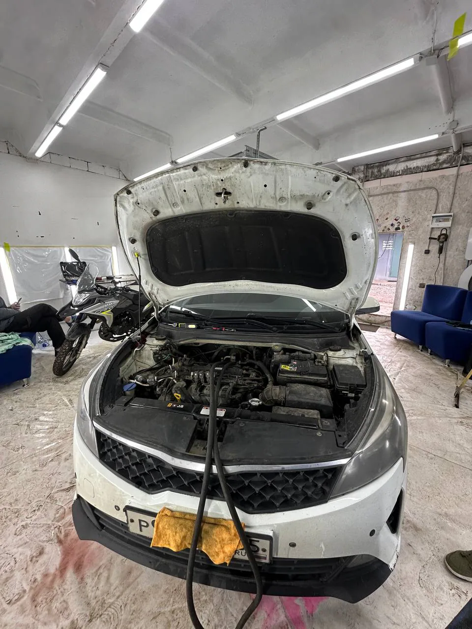 Белый автомобиль с открытым капотом и двумя подключёнными шлангами