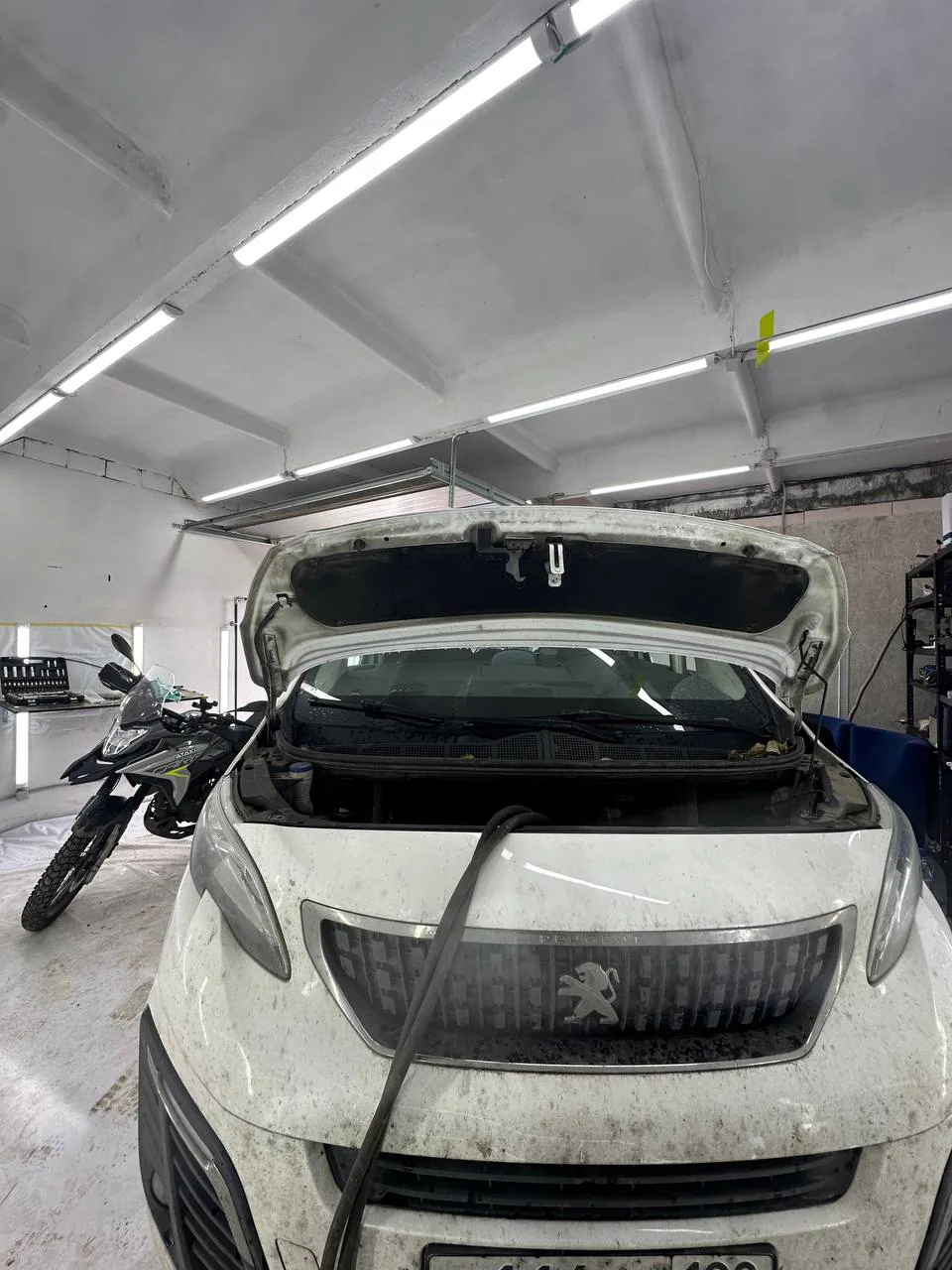 Белый автомобиль Peugeot с открытым капотом и подключённым шлангом